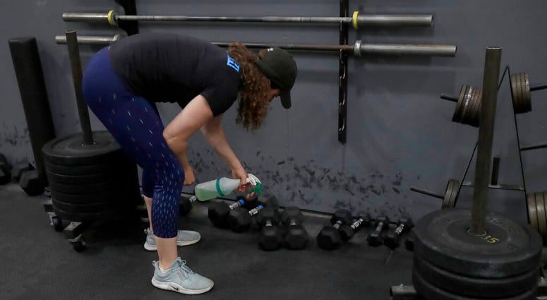FILE - In a Friday, April 24, 2020 file photo, Alexis Garrod, CrossFit Potrero Hill partner and head coach, cleans off weight training equipment in an empty gym, which closed for shelter in place orders over COVID-19 concerns, in San Francisco.
