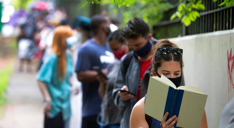 Kelsey Luker reads as she waits in line to vote, Tuesday, June 9, 2020, in Atlanta. Luker said she had been in line for almost two hours.