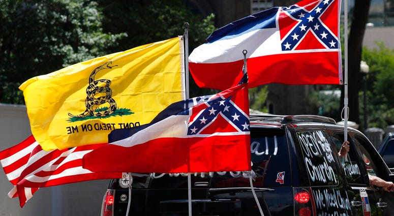 In this April 25, 2020 photo, Mississippi state flags are positioned on a vehicle amid an arrangement with the American flag and a Gadsden flag during a drive-by "re-open Mississippi" protest past the Governor's Mansion, in Jackson, Miss.