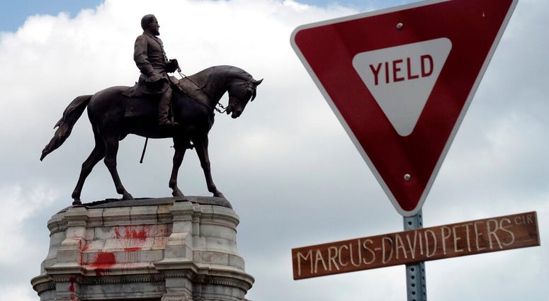 The graffiti-smeared statue of Robert E. Lee and Traveller stand behind a traffic sign with Marcus-David Peters Circle on a handwritten sign below on the circle that surrounds the monument on Monument Avenue in Richmond, Va., Wednesday, June 10, 2020.