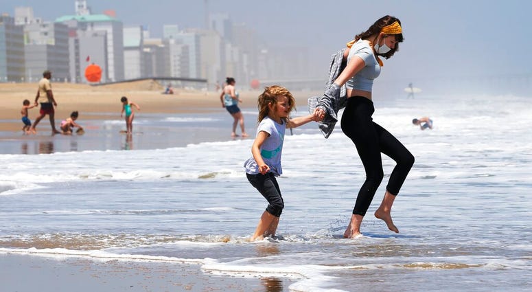 FILE - In this May 22, 2020, file photo, Victoria Faughnan, right, and Evelyn Faughnan, play in the surf in Virginia Beach, Va., the day the state reopened the beachfront during the coronavirus pandemic.