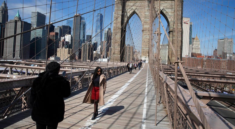 FILE - In this March 16, 2020 file photo, tourist Ines Tshiyomba, center, poses as her friend Garethe Mawonso takes her photo on the Brooklyn Bridge in New York.