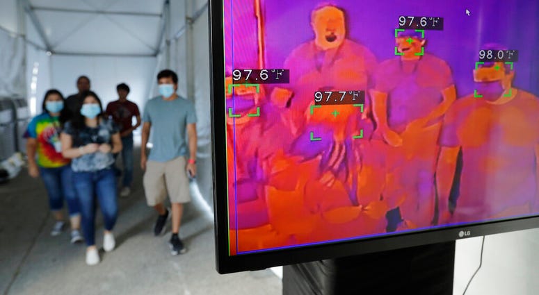 FILE - In this Friday, June 19, 2020 file photo, visitors to Six Flags Fiesta Texas pass through a thermal screening area as they enter the park as a precaution against COVID-19 in San Antonio.