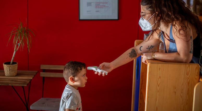 Hugo, 3, has his temperature taken by a teacher as he arrives at Cobi kindergarten in Barcelona, Spain, Friday, June 26, 2020.