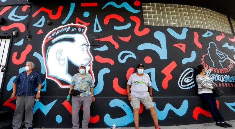 People, social distancing and wearing masks to prevent the spread of the new coronavirus, wait in line at a mask distribution event, Friday, June 26, 2020, in a COVID-19 hotspot of the Little Havana neighborhood of Miami.