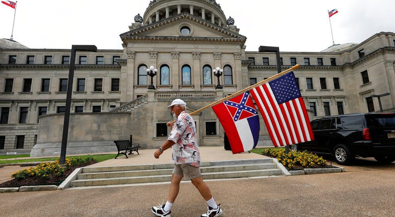 Don Hartness of Ellisville, walks around the Capitol carrying the current Mississippi state flag and the American flag, Saturday, June 27, 2020, in Jackson, Miss.