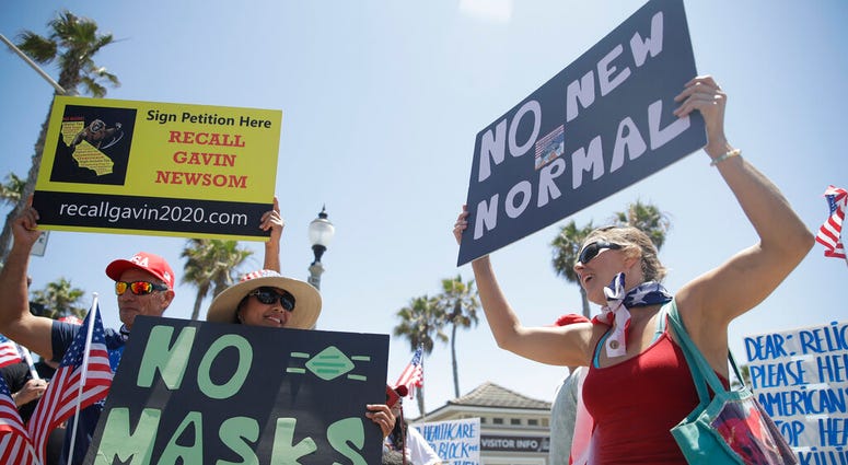 Demonstrators hold signs as they protest the lockdown and wearing masks Saturday, June 27, 2020, in Huntington Beach, Calif.