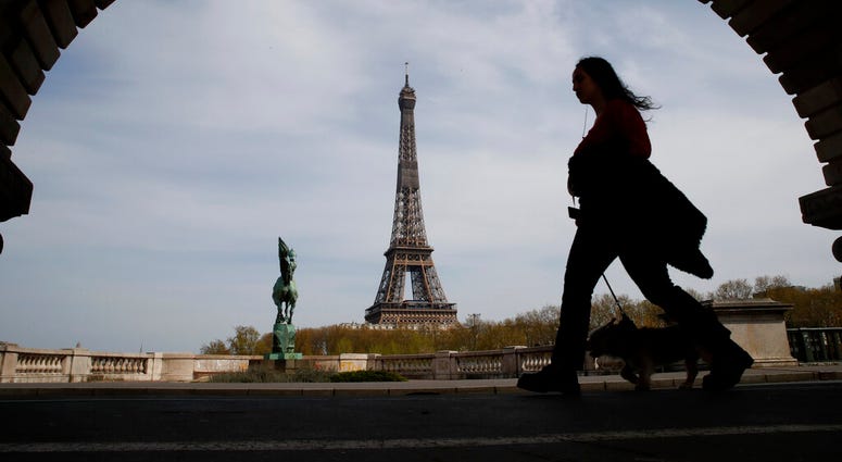 FILE - In this Tuesday, April 7, 2020 file photo, a woman walks her dog on a Paris bridge, with the Eiffel tower in background, during a nationwide confinement to counter the COVID-19.