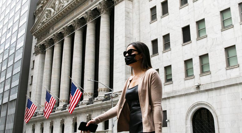 A woman wearing a mask passes the New York Stock Exchange, Tuesday, June 30, 2020, during the coronavirus pandemic.