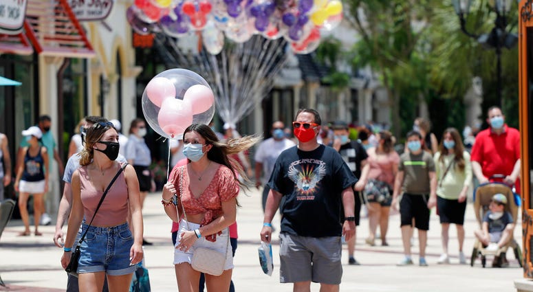 FILE - In this June 16, 2020, file photo, guests required to wear masks because of the coronavirus stroll through the Disney Springs shopping, dining and entertainment complex in Lake Buena Vista, Fla.