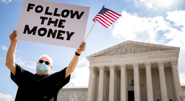 Bill Christeson holds up a sign that reads "Follow the Money" outside the Supreme Court, Thursday, July 9, 2020, in Washington.