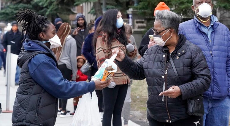 FILE - In this April 7, 2020, file photo, a worker hands out disinfectant wipes and pens as voters line up outside Riverside High School for Wisconsin's primary election in Milwaukee.