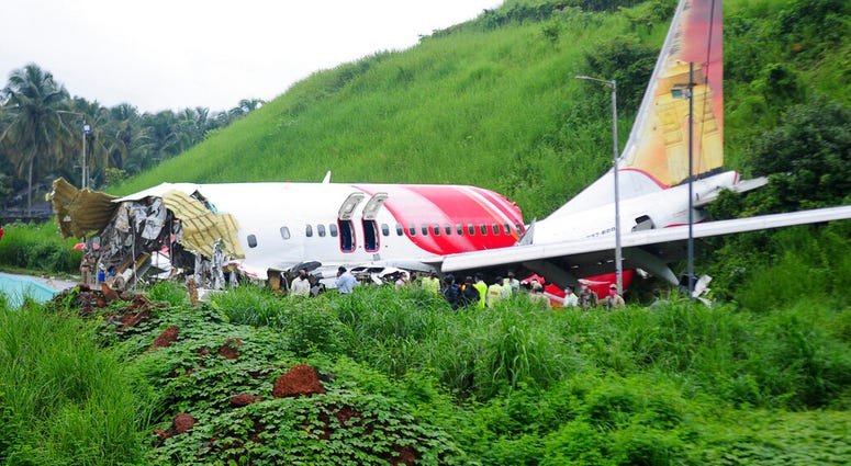 Officials stand on the debris of the Air India Express flight that skidded off a runway while landing in Kozhikode, Kerala state, India, Saturday, Aug. 8, 2020.