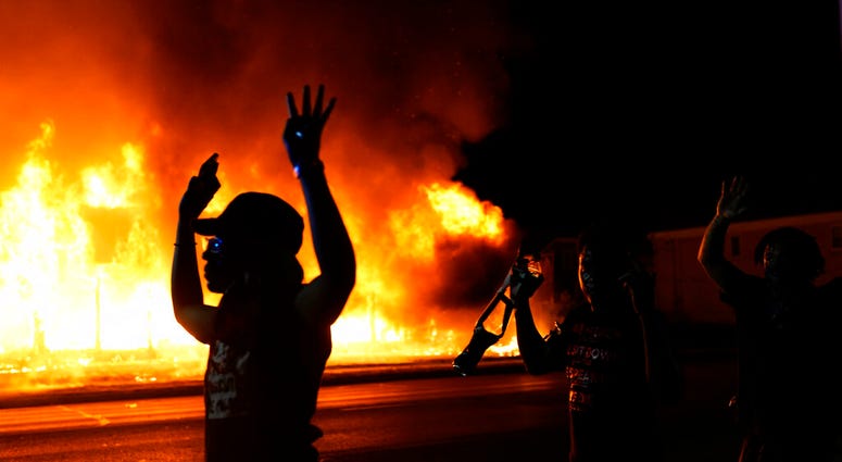 Protesters walk past police with their arms up, late Monday, Aug. 24, 2020, in Kenosha, Wis., as a building burns in the background. Protests have erupted following the police shooting of Jacob Blake a day earlier. (AP Photo/David Goldman) Protesters walk past police with their arms up, late Monday, Aug. 24, 2020, in Kenosha, Wis., as a building burns in the background. Protests have erupted following the police shooting of Jacob Blake a day earlier. (AP Photo/David Goldman)