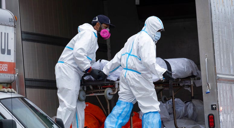 FILE - In this April 29, 2020, file photo, workers move bodies to a refrigerated truck from the Andrew T. Cleckley Funeral Home in the Brooklyn borough of New York. (AP Photo/Craig Ruttle) FILE - In this April 29, 2020, file photo, workers move bodies to a refrigerated truck from the Andrew T. Cleckley Funeral Home in the Brooklyn borough of New York. (AP Photo/Craig Ruttle)