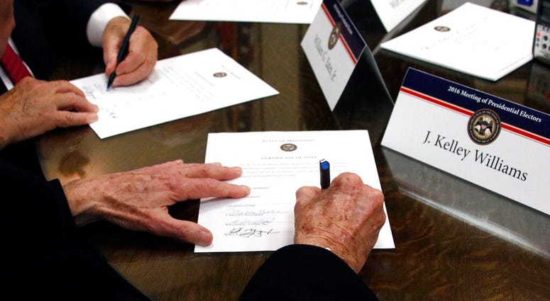 FILE - In this Dec. 19, 2016, file photo members of the Mississippi Electoral College sign certificates of vote in the process of formally casting their electoral votes in the 2016 General Election
