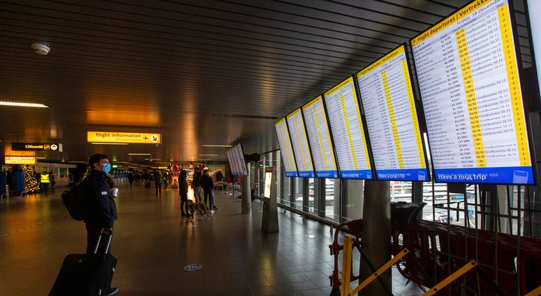 FILE- In this Friday Dec. 18, 2020, file photo, A traveller wearing a face mask checks the flight departures at Schiphol Airport, near Amsterdam, Netherlands.