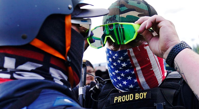 FILE - In this Sept. 26, 2020, file photo, member of the Proud Boys, right, stands in front of a counter protester as members of the Proud Boys and other right-wing demonstrators rally, in Portland.