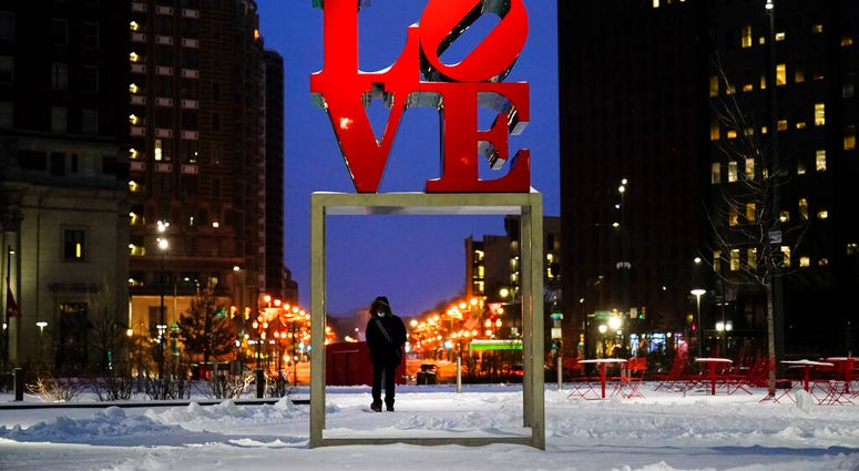 A person wearing a face mask as a precaution against the coronavirus walks during a winter storm near the Robert Indiana sculpture "LOVE" at John F. Kennedy Plaza, commonly known as Love Park, in Philadelphia, Monday, Feb. 1, 2021.