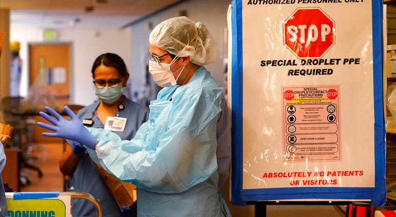 FILE - In this Jan. 26, 2021, file photo, registered nurse Diane Miller pulls on gloves and other protective equipment as she prepares to enter patient rooms in the COVID acute care unit at UW Medical Center-Montlake in Seattle.