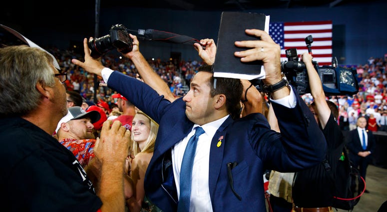 ADDS THAT MAN BLOCKING CAMERA IS A VOLUNTEER - A volunteer member of the advance team for President Donald Trump blocks a camera as a photojournalist attempts to take a photo of a protester during a campaign rally at the Ford Center, Thursday, Aug. 30, 20