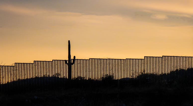 US -Mexico border wall at sunset with iconic saguaro cactus - stock photo