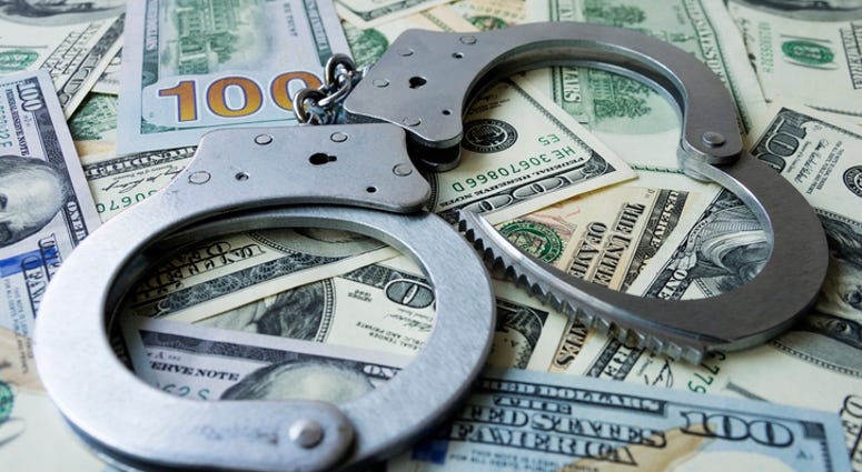 Handcuffs on a pile of US dollar banknotes- symbolic image of a bribe, laundering of money or corruption.