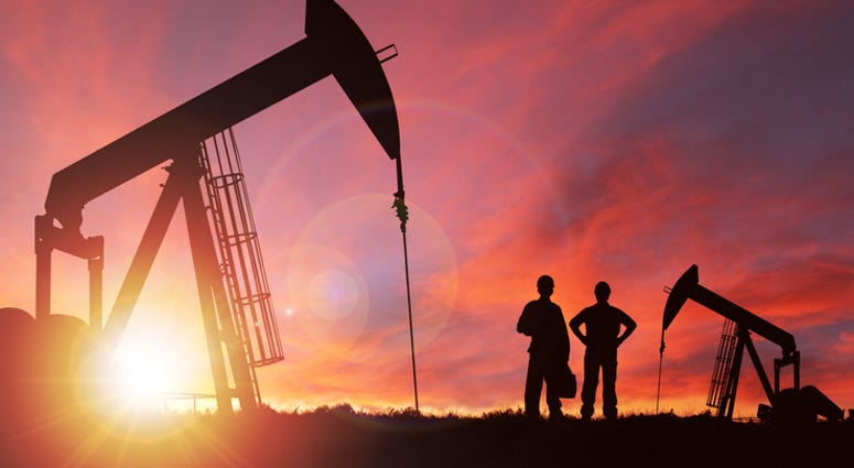 Pump jack silhouette and hard hat workers against a sunset sky with deliberate lens flare and copy space. These jacks can extract between 5 to 40 liters of crude oil and water emulsion at each stroke.