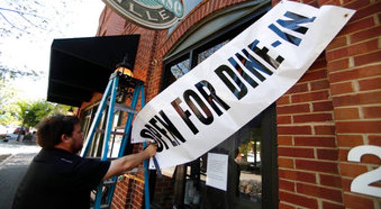 FILE - In this April 27, 2020, file photo, Jason Godbey hangs a banner over the entrance of Madison Chop House Grille as they prepare to shift from take out only to dine-in service in Madison, Ga. (AP Photo/John Bazemore, File) FILE - In this April 27, 2020, file photo, Jason Godbey hangs a banner over the entrance of Madison Chop House Grille as they prepare to shift from take out only to dine-in service in Madison, Ga. (AP Photo/John Bazemore, File)