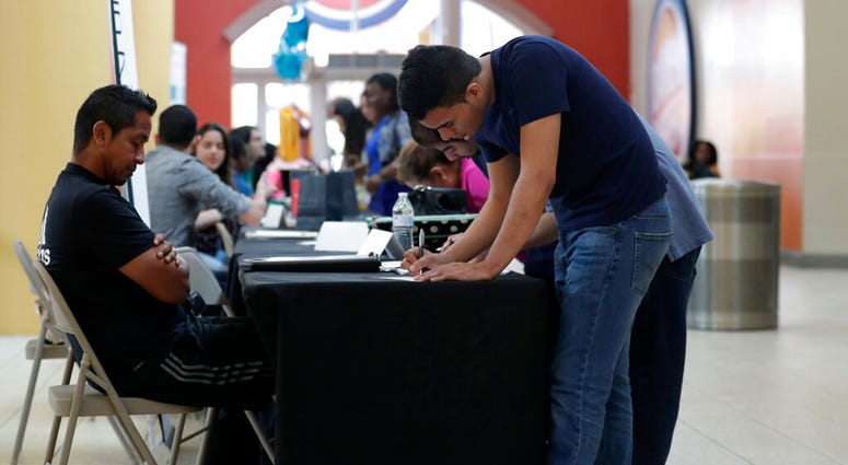 FILE - In this Oct. 1, 2019, file photo Billy Ramos, right, fills out a job application with Adidas during a job fair at Dolphin Mall in Miami. On Friday, Nov. 1, the U.S. government issues the October jobs report. (AP Photo/Lynne Sladky)