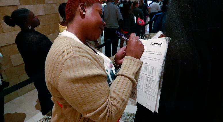 In this June 4, 2019 photo, job applicant Esta Williams, center, uses Tracy Simeton's back to fill out a questionnaire as they wait in line at the Seminole Hard Rock Hotel & Casino Hollywood during a job fair in Florida. (AP Photo/Wilfredo Lee, File)
