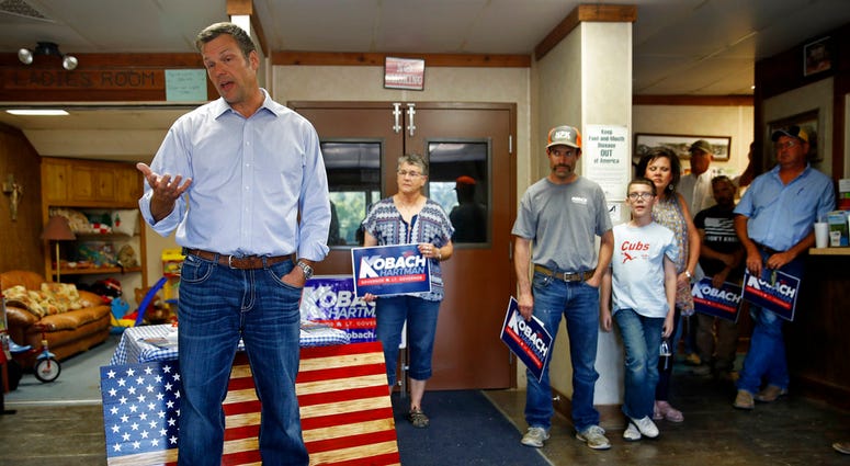Kansas Secretary of State Kris Kobach, left, and candidate for the Republican nomination for Kansas Governor addresses supporters during a campaign stop Friday, Aug. 3, 2018, at the Fort Scott Livestock Market in Fort Scott, Kan. (AP Photo/Charlie Riedel)