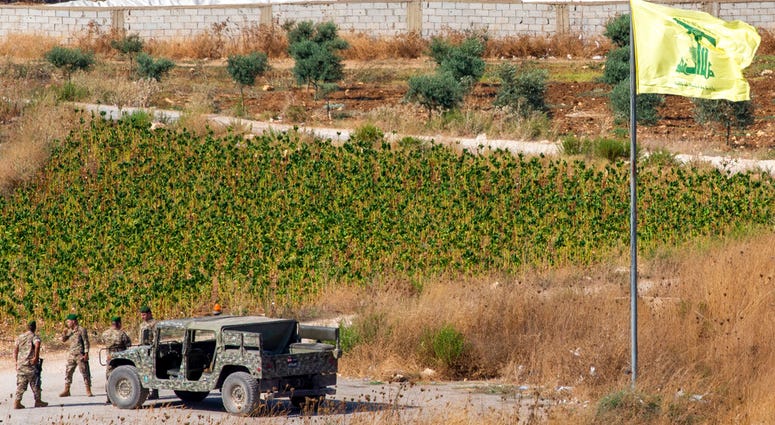 Lebanese soldiers next to a Hezbollah flag patrol in the southern Lebanese village of Aitaroun, on the Israel-Lebanon border, Israel, Tuesday, Aug. 27, 2019. (AP Photo/Ariel Schalit)
