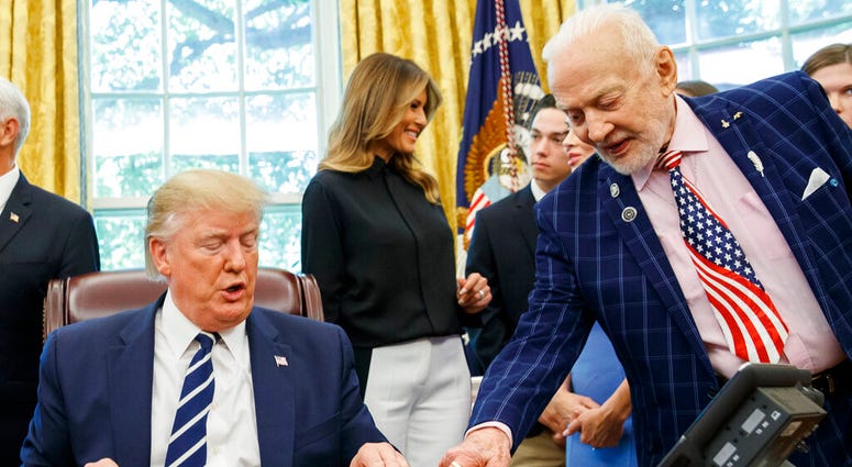 President Donald Trump receives a gift from Apollo 11 astronaut Buzz Aldrin, with first lady Melania Trump, during a photo opportunity commemorating the 50th anniversary of the Apollo 11 moon landing in the Oval Office. (AP Photo/Alex Brandon)