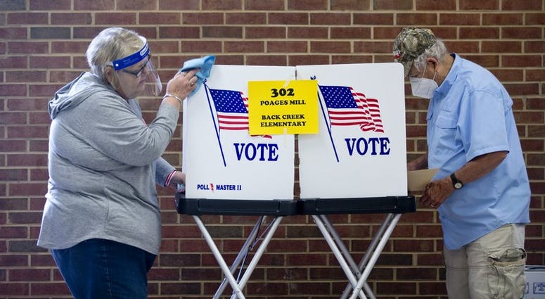 Glenda Patsel, left, wipes down a voting booth as Bobby J. Lambert fills out his ballot for the senate Republican candidates primary election, Tuesday, June 23, 2020, at Hidden Valley Middle School in Roanoke, Va.