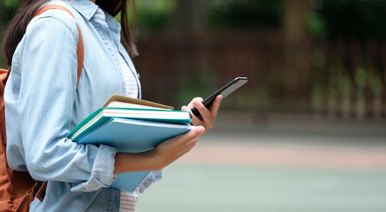 Girl holding books and smartphone while walking in school campus background - stock photo. iStock / Getty Images Plus