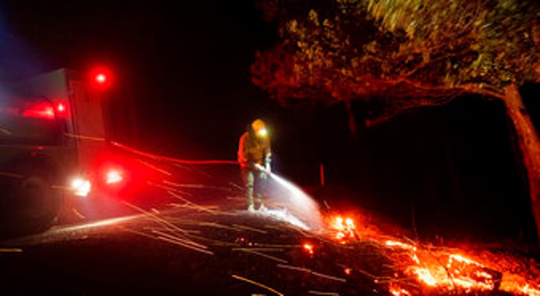 A firefighter battling the Kincade fire extinguishes a hot spot as strong winds send embers flying in Calistoga, Calif., on Tuesday, Oct. 29, 2019. (AP Photo/Noah Berger)