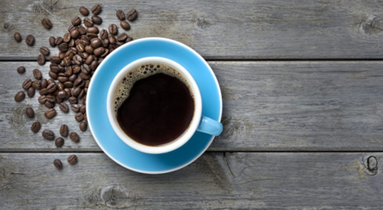A blue coffee cup full of black coffee on a wood background with coffee beans