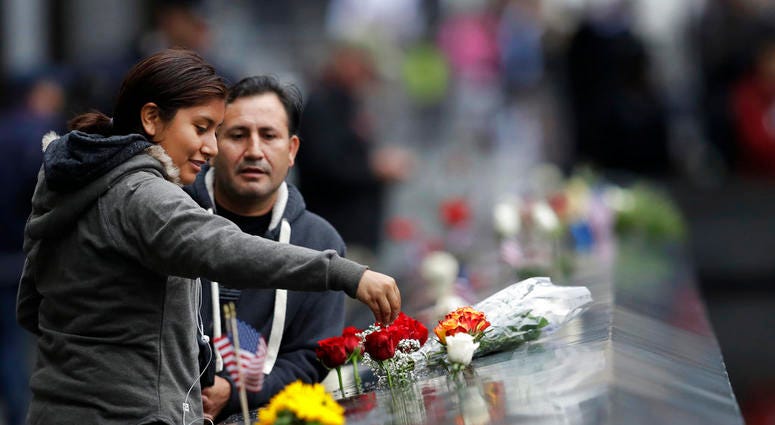 A woman drips water on a bouquet of flowers at the North Pool during a ceremony marking the 17th anniversary of the terrorist attacks on the United States on Tuesday, Sept. 11, 2018, in New York. (AP Photo/Mark Lennihan)