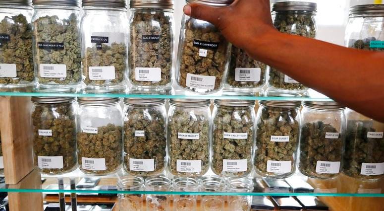 In this Tuesday, Oct. 2, 2018, photo, a clerk reaches for a container of marijuana buds for a customer at Utopia Gardens, a medical marijuana dispensary, in Detroit.
