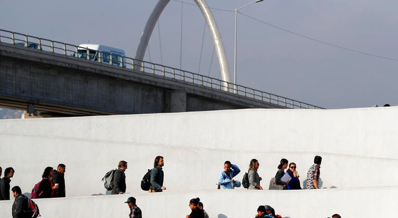 FILE - In this Tuesday, March 19, 2019, file photo, a man who only gave his first name as Ariel, of Honduras, center in blue shirt, crosses into the United States to begin his asylum case with others after being returned to Mexico in Tijuana, Mexico. A U.