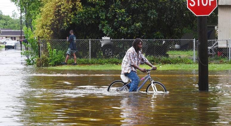 A man tries to bike through the flooding from the rains of storm Barry on LA Hwy 675 in New Iberia, La., Sunday, July 14, 2019. (Henrietta Wildsmith/The Shreveport Times via AP)