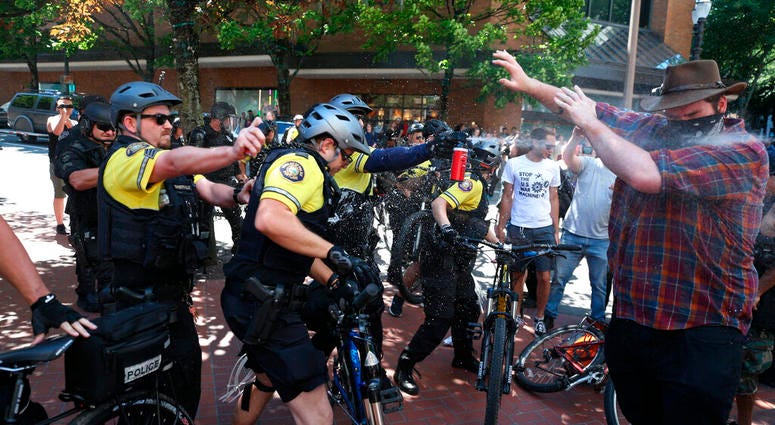 In this June 29, 2019, file photo, after a confrontation between authorities and protesters, police use pepper spray as multiple groups, including Rose City Antifa, the Proud Boys and others protest in Portland. (Dave Killen/The Oregonian via AP, File)