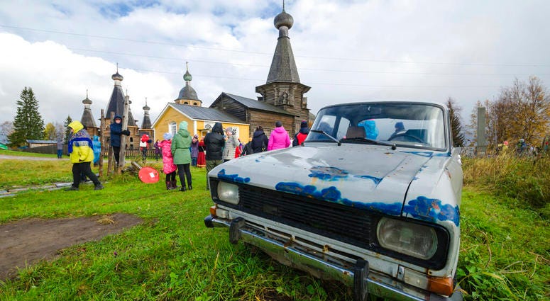 In this photo taken on Oct. 7, 2018, people walk the street with the 18th century Trinity Church in the background in the village of Nyonoksa, northwestern Russia. (AP Photo/Sergei Yakovlev)