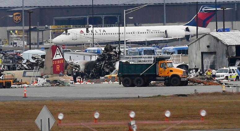 A Delta commercial airline plane taxis to take-off behind investigators at the wreckage of World War II-era bomber plane that crashed at Bradley International Airport in Windsor Locks, Conn., Wednesday, Oct. 2, 2019.