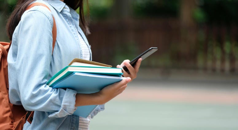Girl holding books and smartphone while walking in school campus background - stock photo. iStock / Getty Images Plus