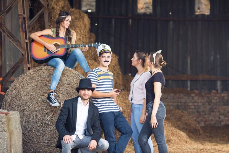 Group of friends wear costumes around a bale of hay