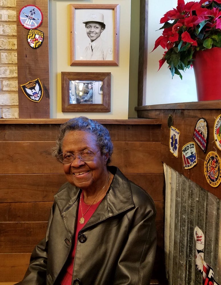 World War II Army 1st Lt. Vivian “Millie” Bailey sits at a table that honors her at a Maryland Mission BBQ restaurant. On the wall above her is her service photo.