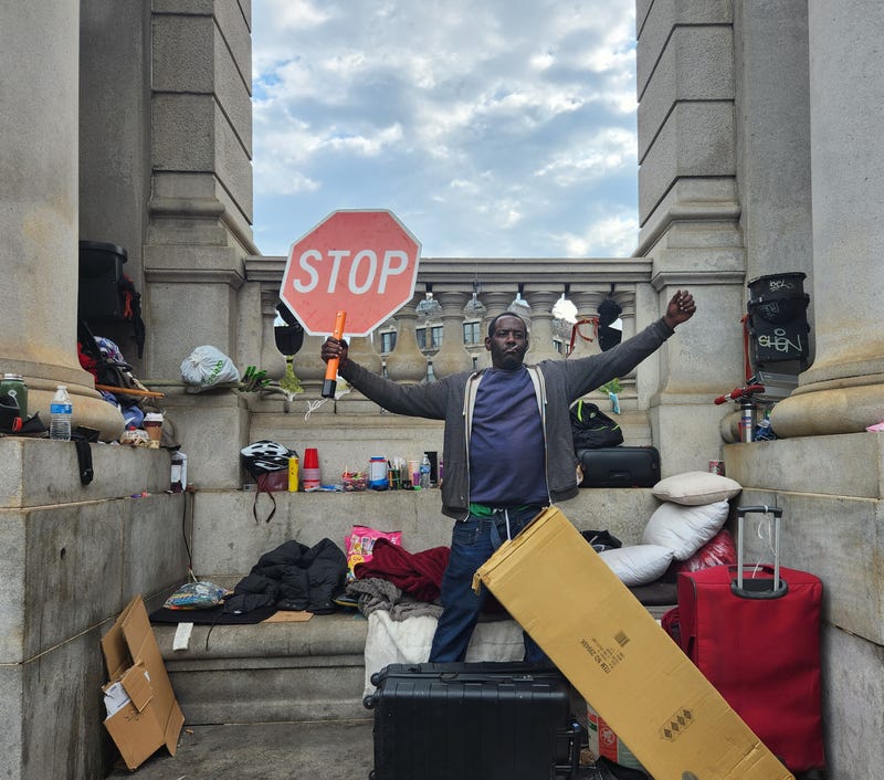 A homeless man defiantly raises a stop sign after police and sanitation workers force him to dismantle his makeshift tarp shelter at the base of the Manhattan bridge.