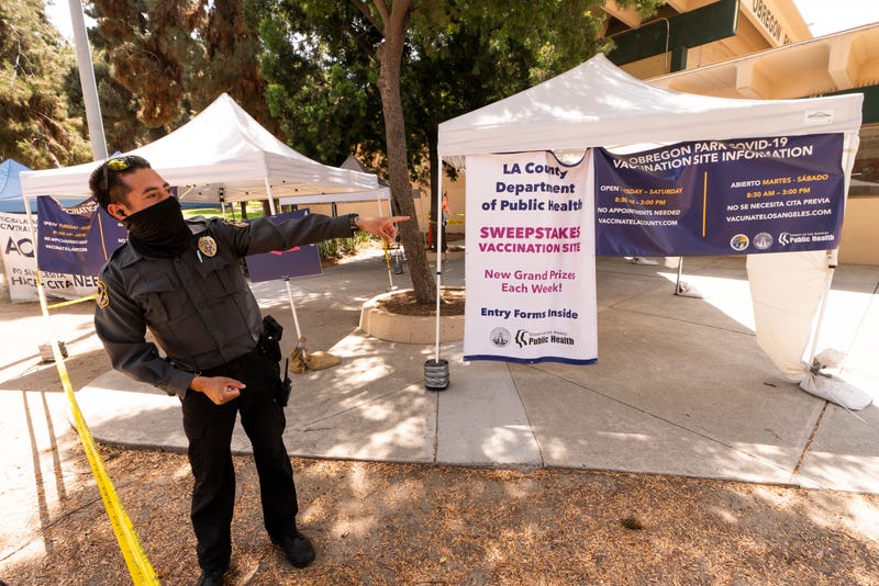A private security guard gives directions to people looking to get vaccinated, as banners advertise the availability of the Johnson & Johnson and Pfizer COVID-19 vaccines at a county-run vaccination site offering free walk-in with no appointment needed at the Eugene A. Obregon Park in Los Angeles Thursday, July 22, 2021. The top health official in Los Angeles County on Thursday implored residents to get vaccinated as the region experiences a coronavirus surge similar to last summer's. (AP Photo/Damian Dovarganes)